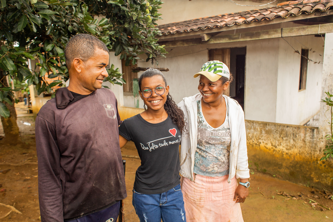 Um jovem negra dá risada ao lado de seus pais em um cenário rural