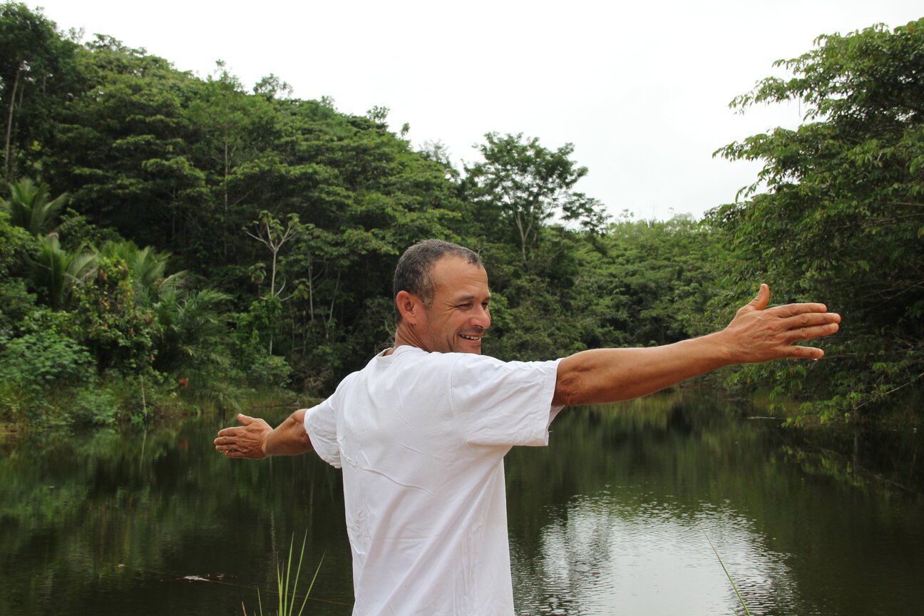 Um homem está com os braços abertos e sorrindo em frente a um rio.